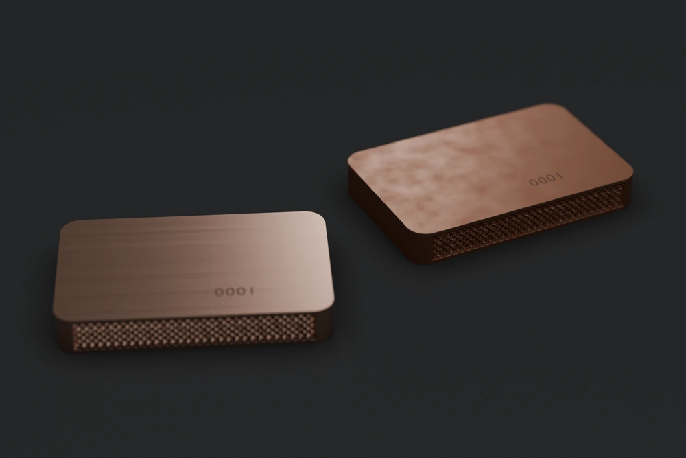 Render of two copper Keys engraved 0001 lying on a dark surface. The left one is bright and new. The right one is darker and browner after two weeks of use. Both have diamond-knurled edges.